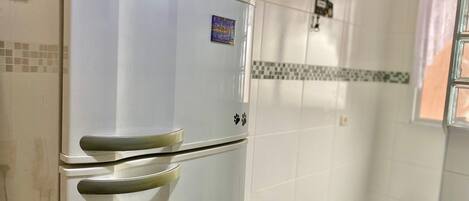 A white Electrolux refrigerator in a kitchen with tiled walls and a checkered floor.