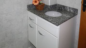 Een badkamer met een granieten aanrechtblad, een witte wastafel en een houten bloevas.