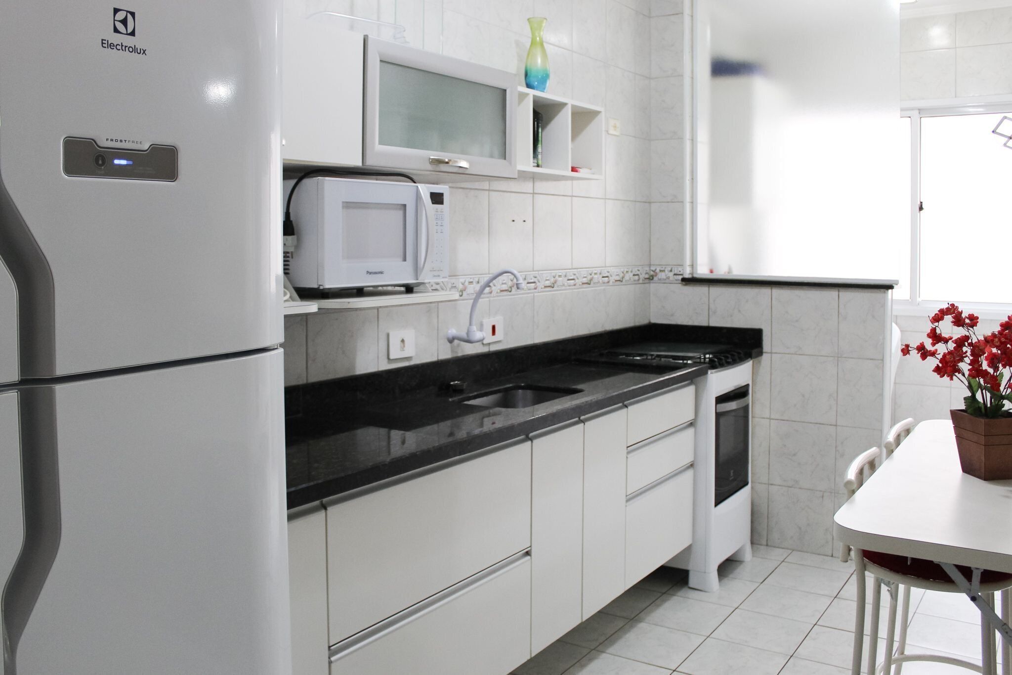 Una cocina moderna con armarios blancos, microondas integrado, un lavamanos y un comedor con mesa y sillas.