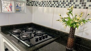 A kitchen with a gas stove, a vase with flowers, and a tiled backsplash. - Residencial Blaia  (Praia Grande)