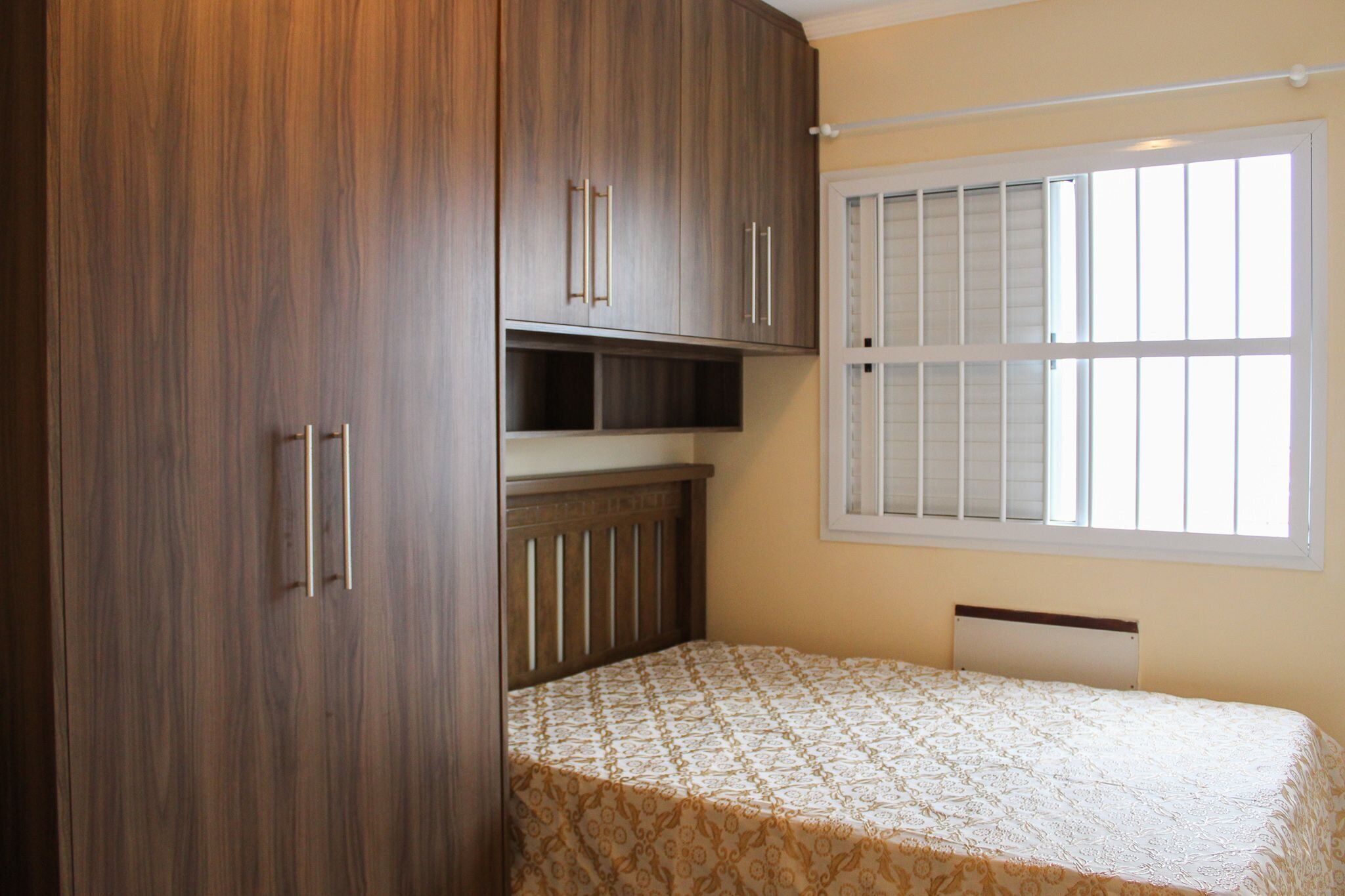 Quarto com cama, guarda-roupa de madeira e janela com persianas.