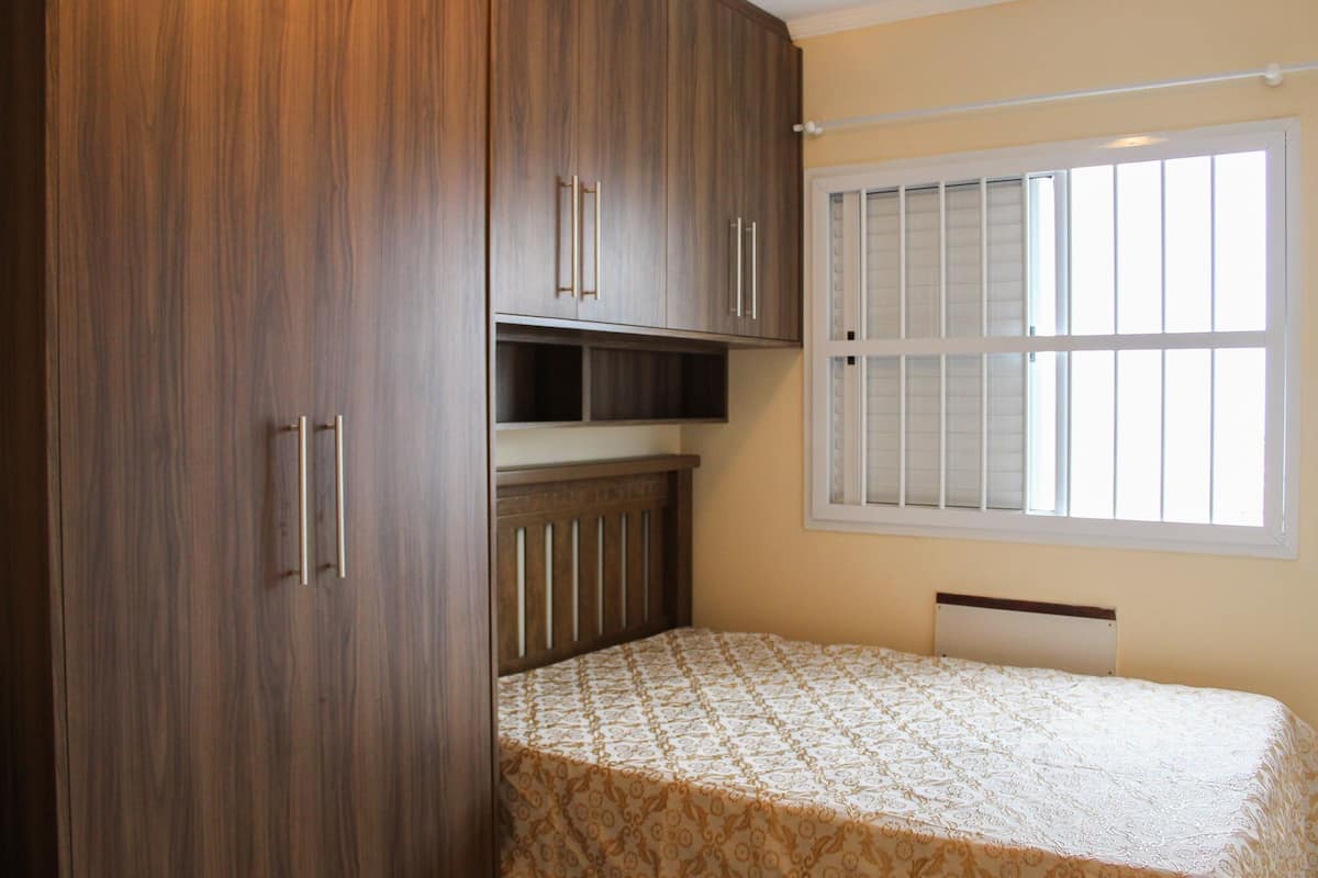A bedroom with a bed, wooden wardrobe, and a window with blinds.