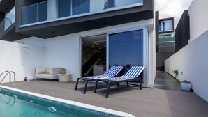 A modern outdoor pool area with a lounge chair and a sofa, a staircase leading to an upper level, and a potted plant. - Casa com Vista Fabulosa Sobre a Baía do Funchal, a 5mt (Funchal)