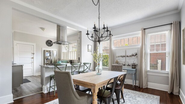 A spacious dining area with a wooden table and chairs, a chandelier, and a view of the kitchen and living area.