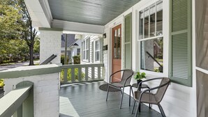 A porch with a white railing, two wicker chairs, and a door with green shutters.