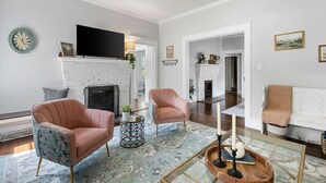 A living room with a fireplace, two armchairs, a coffee table, and a television mounted above the fireplace.