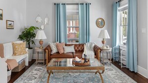 A living room with a brown leather sofa, a glass coffee table, a white armchair, and a blue patterned rug.
