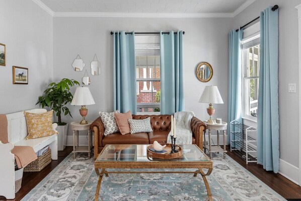Un salon avec un canapé en cuir marron, une table basse en verre, un fauteuil blanc et un tapis à motifs bleus.