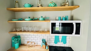 Una cocina con estantes de madera, un microondas y diversos utensilios de cocina.