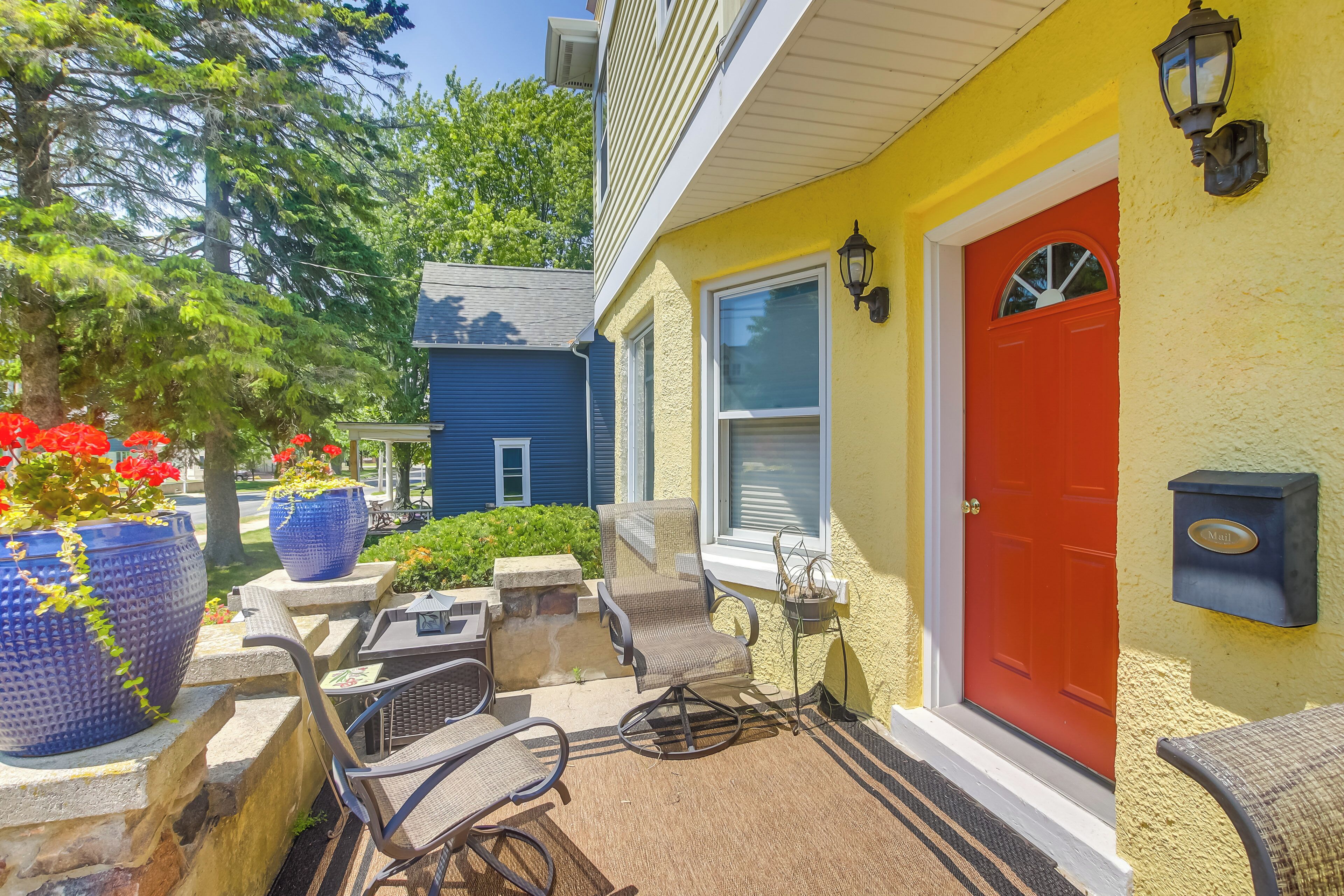 A yellow house with a red door, outdoor seating, and potted plants.