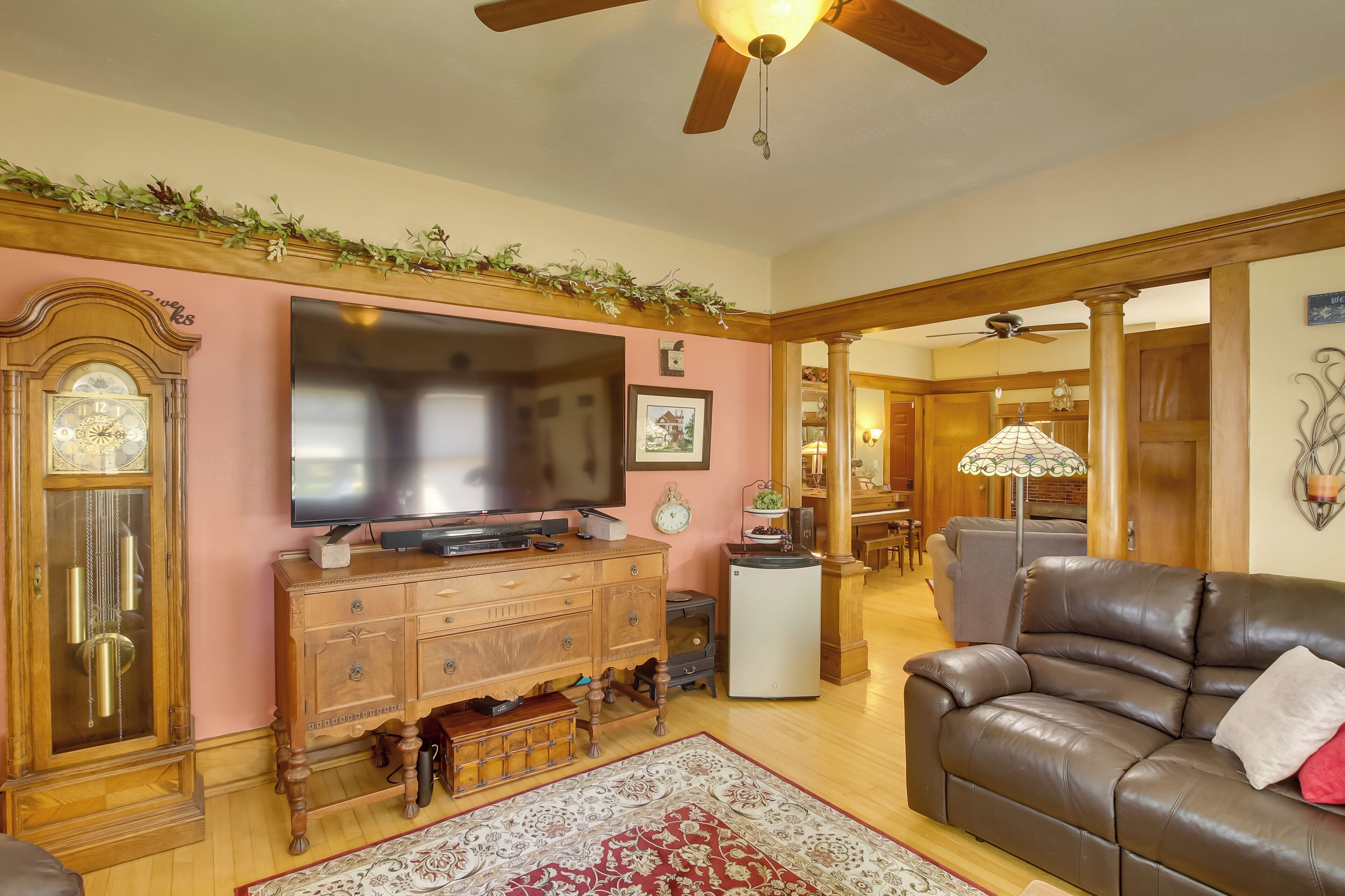 A living room with a wooden TV stand, a brown leather sofa, a patterned rug, and a ceiling fan.
