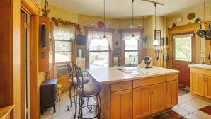 A kitchen with wooden cabinets, a central island, pendant lights, and a view of the outdoors. - Algoma Victorian - Steps to Lake Michigan! (Algoma)