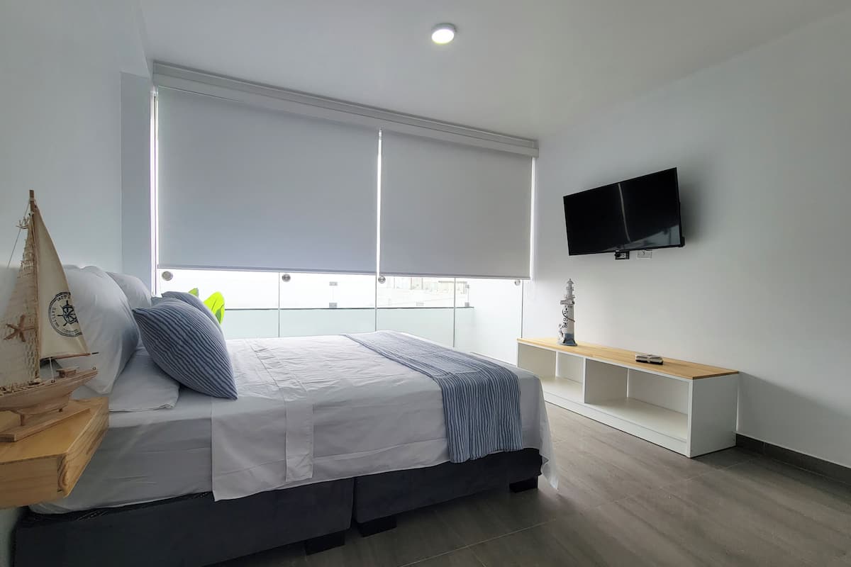 A modern bedroom with a bed, a TV, and a window with blinds.