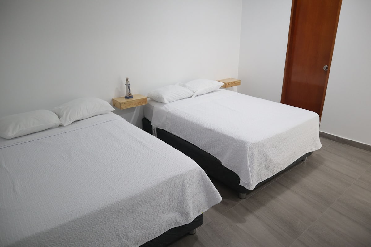 Two single beds with white linens in a room with a wooden floor and a wooden door.