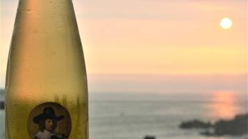 Una botella de vino Faustino V y una porción de pastel en un plato, con vista al océano y al atardecer de fondo.