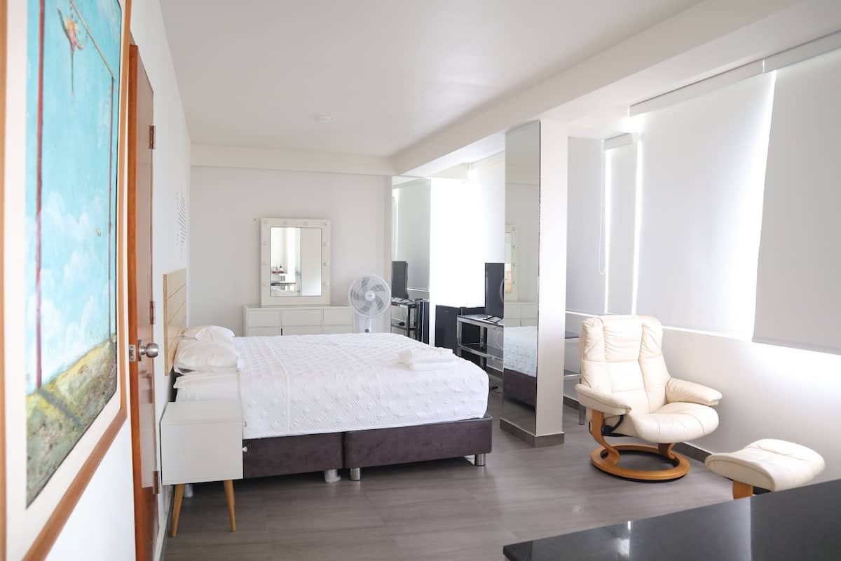 A modern bedroom with a bed, bedside table, chair, and a large mirror.