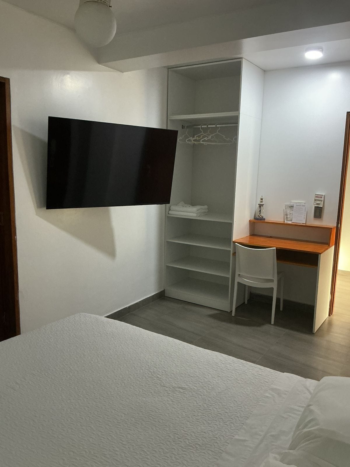 A bedroom with a bed, a desk with a chair, a wardrobe, and a mounted television.