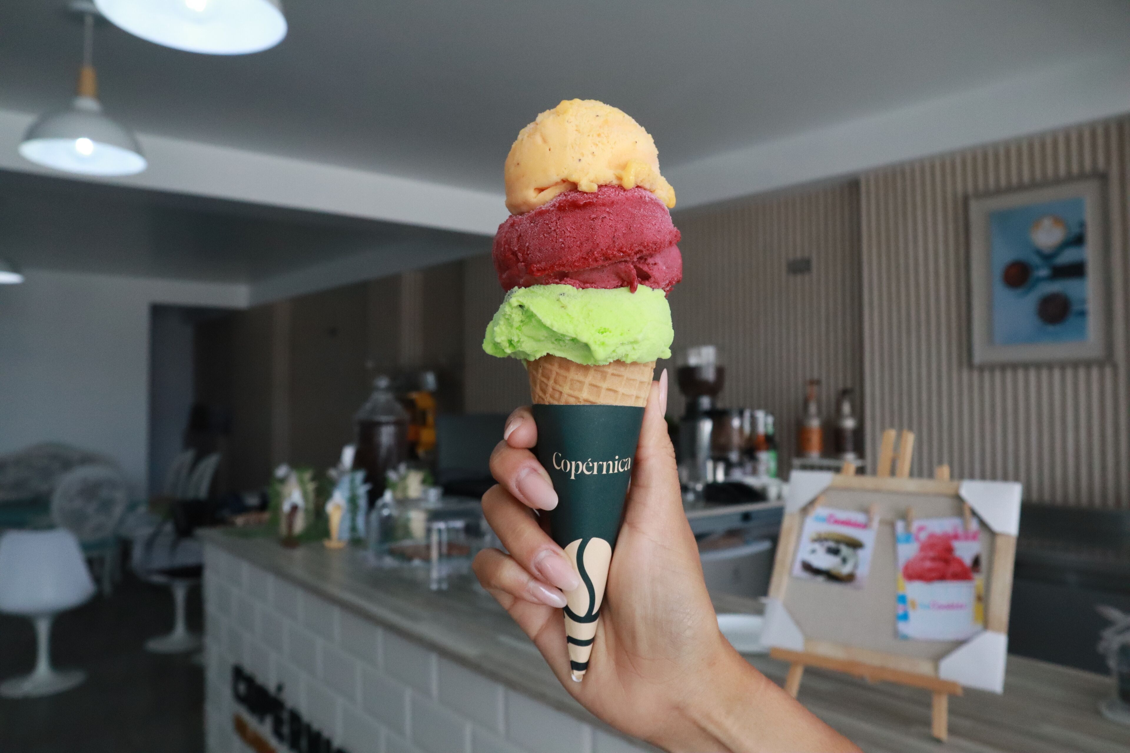 Una mano sostiene un cono de gofre con tres bolas de helado.