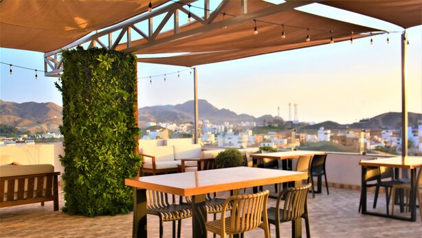 An outdoor seating area with tables and chairs, a green vertical garden, and a view of a cityscape with mountains in the background.