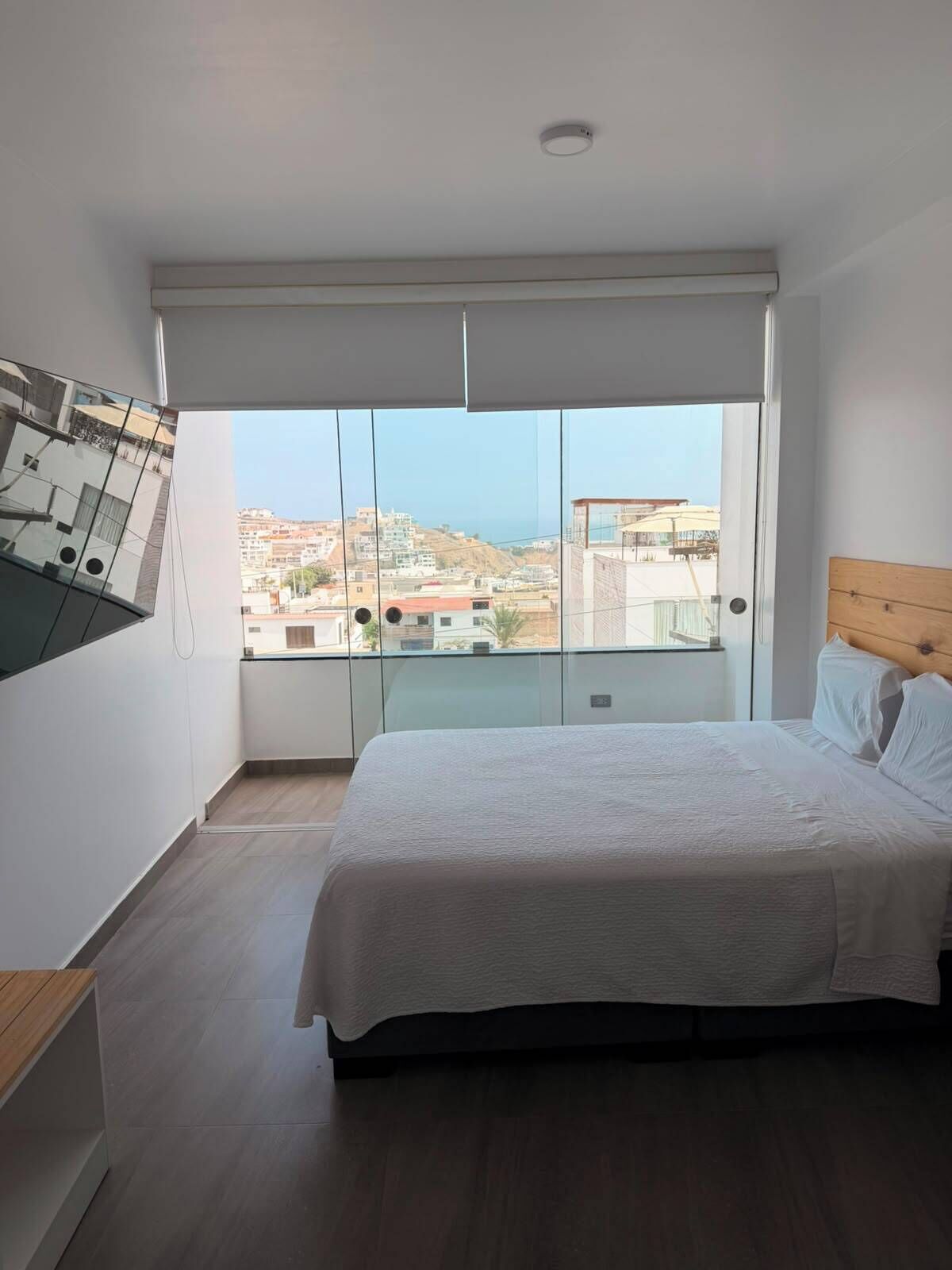 A bedroom with a large bed, a view of the city through floor-to-ceiling windows, and a wooden headboard.