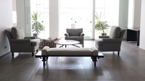 Een moderne woonkamer met twee banken, een salontafel en een lange bank. Twee potplanten en een groot raam met uitzicht op gebouwen.
