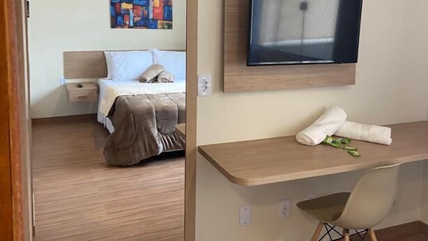 A hotel room with a bed, a desk, a TV, and a painting on the wall. - POUSADA HD (Nova Friburgo)