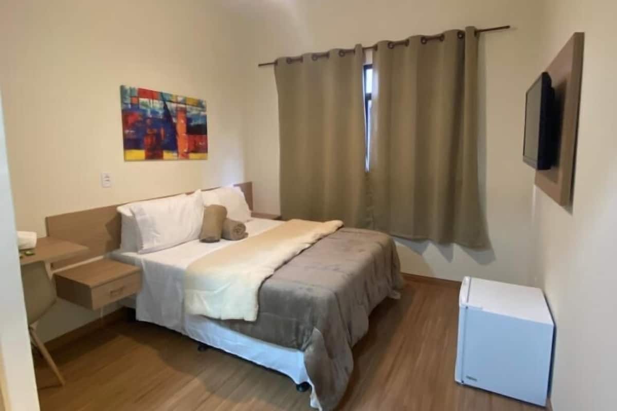 A bedroom with a bed, bedside table, TV, and a painting on the wall.