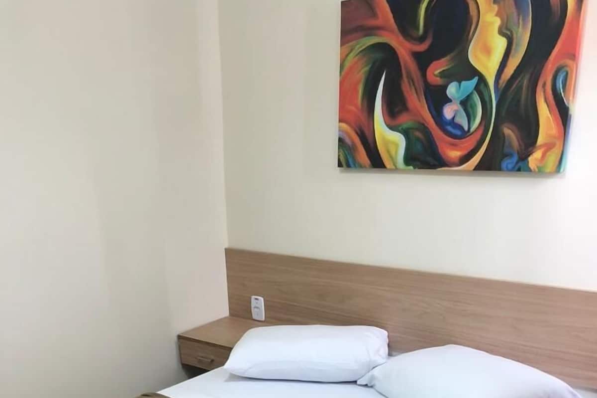 A hotel room with a bed, a nightstand, and a wall-mounted abstract painting.