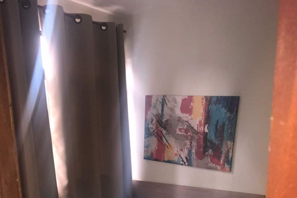 A hotel room with a bed, curtains, and a colorful abstract painting on the wall.
