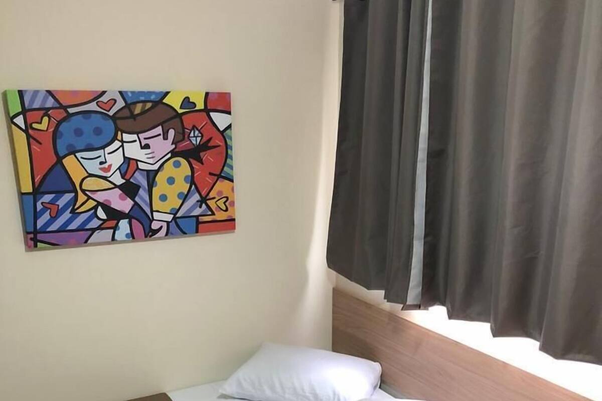 A small, neatly arranged bedroom with a single bed, a bedside table, a small desk, and a colorful abstract painting on the wall.