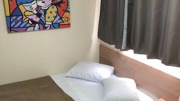 Un dormitorio pequeño y ordenado con una cama individual, una mesita de noche, un escritorio pequeño y un cuadro abstracto y colorido en la pared.