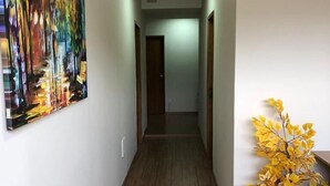 A hallway with wooden flooring, a painting on the left wall, and a potted plant on the right. - POUSADA HD (Nova Friburgo)