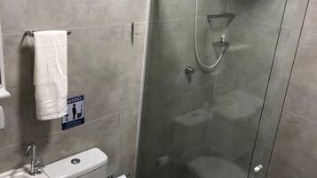 Un baño moderno con ducha de vidrio, inodoro, lavamanos y toallero.