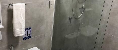 Un baño moderno con ducha de vidrio, inodoro, lavamanos y toallero.