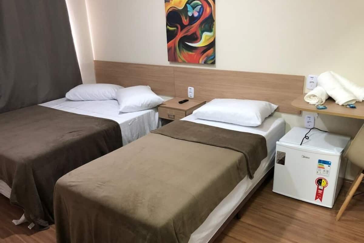A hotel room with two single beds, a nightstand, a small refrigerator, and a painting on the wall.