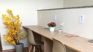 A dining area with a wooden table, two chairs, a potted plant with yellow leaves, a small flower pot, and a bottle of alcohol. - POUSADA HD (Nova Friburgo)