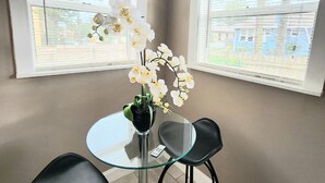 Une pièce d’angle avec deux fenêtres, une table en verre avec des chaises et un pot d’orchidée.