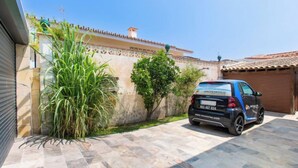 A car parked in a driveway with a tiled patio, a wall with a decorative pattern, and a clear blue sky.