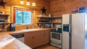 Et køkken med træskabe, mikroovn, komfur, køleskab og et vindue med gardiner.