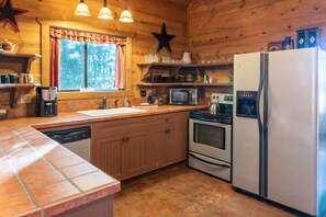 Una cocina con armarios de madera, microondas, estufa, refrigerador y una ventana con cortinas.