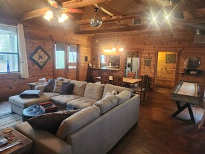 Un acogedor interior de cabaña de madera con un sofá seccional, una mesa de comedor y una mesa de billar.