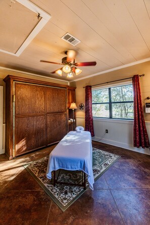 A room with a bed, a wooden cabinet, a ceiling fan, a window with curtains, and a radiator.