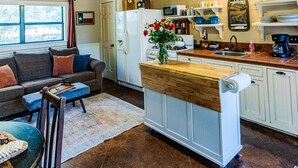 Un vaste espace de vie comprenant une cuisine, des poutres apparentes, un ventilateur de plafond et une table à manger avec des chaises.