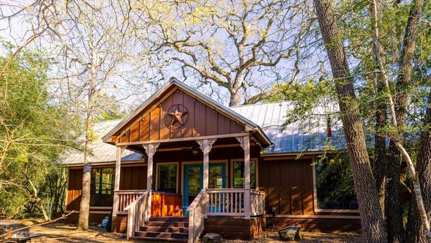 Une cabane en bois dotée d’un porche, entourée d’arbres et bordée d’une allée en gravier.