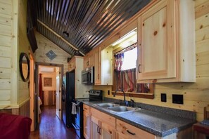 A compact kitchen with wooden cabinets, a granite countertop, a microwave, and a sink.