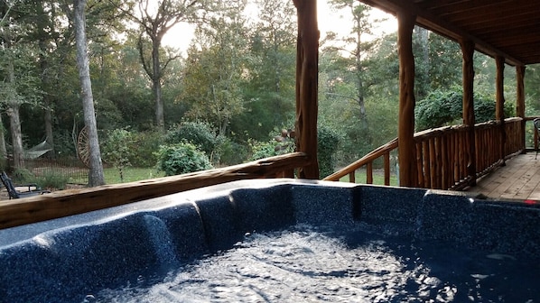 A hot tub with a wooden deck and a view of a forested area.