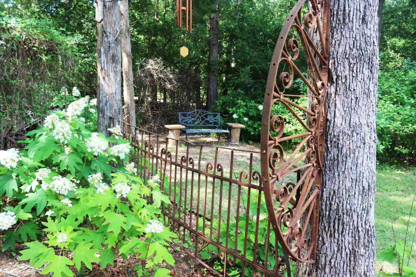 Una valla metálica rústica, un banco de madera y un árbol en un jardín.