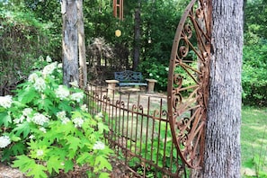 A rustic metal fence, a wooden bench, and a tree in a garden setting.