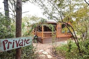 A wooden cabin with a porch, surrounded by trees and a sign indicating it is private.
