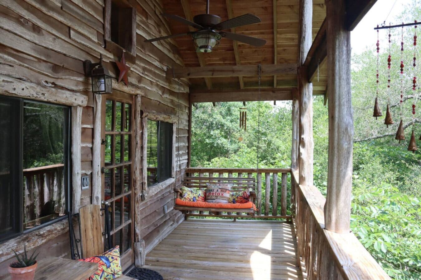 Une cabane en bois avec une véranda, un ventilateur de plafond et une vue sur la forêt.